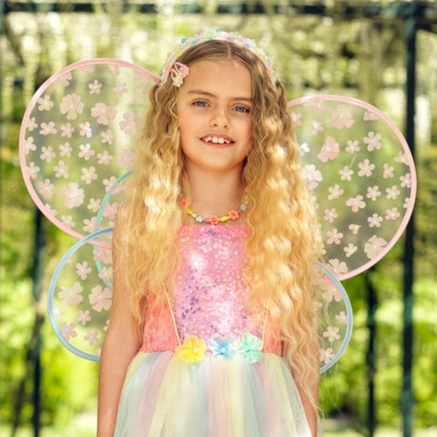 Young girl in a fairy costume with floral wings standing outdoors.