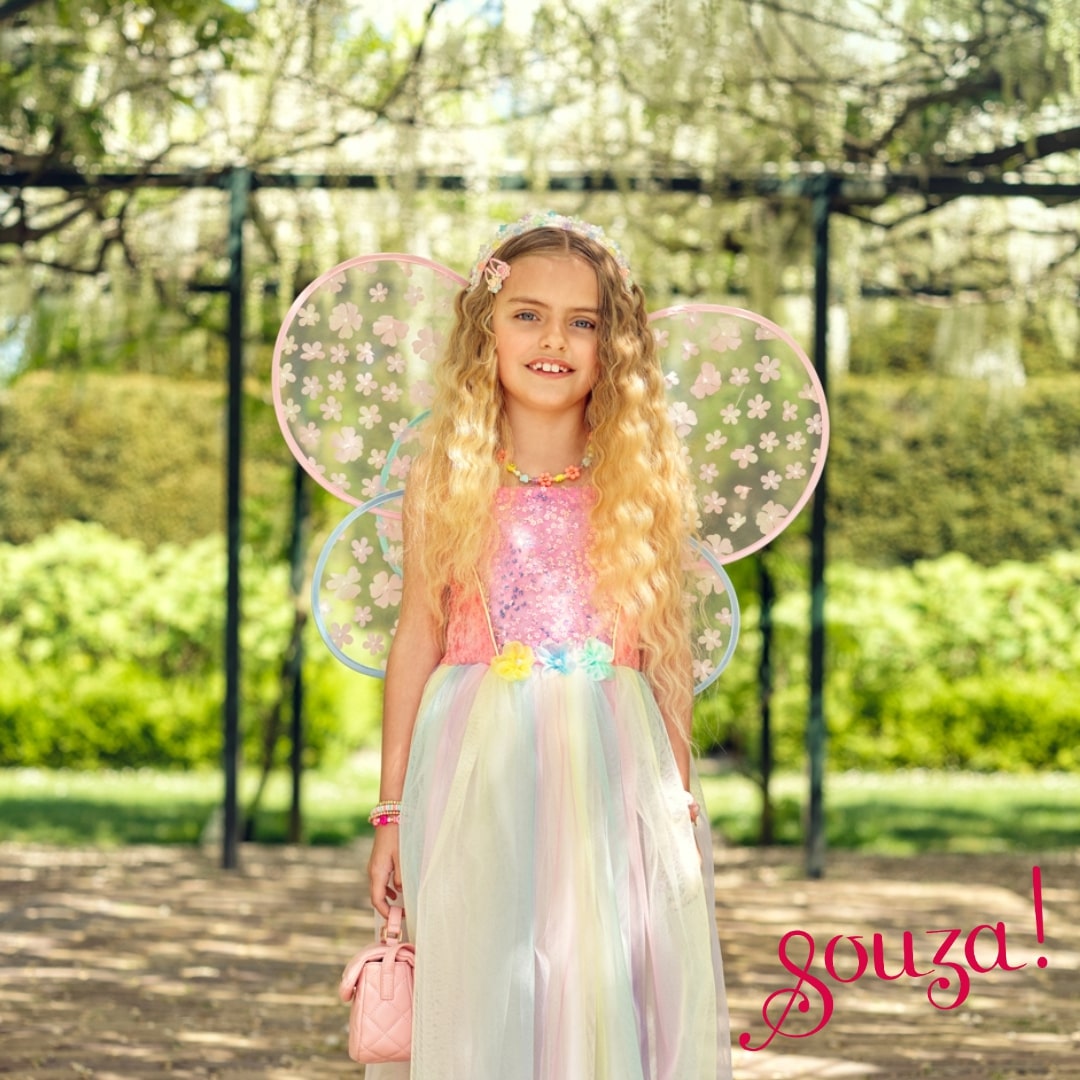 Young girl in a fairy costume with floral wings standing outdoors.