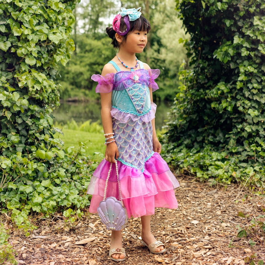 Young girl in a colorful dress standing in a garden with greenery and a path.