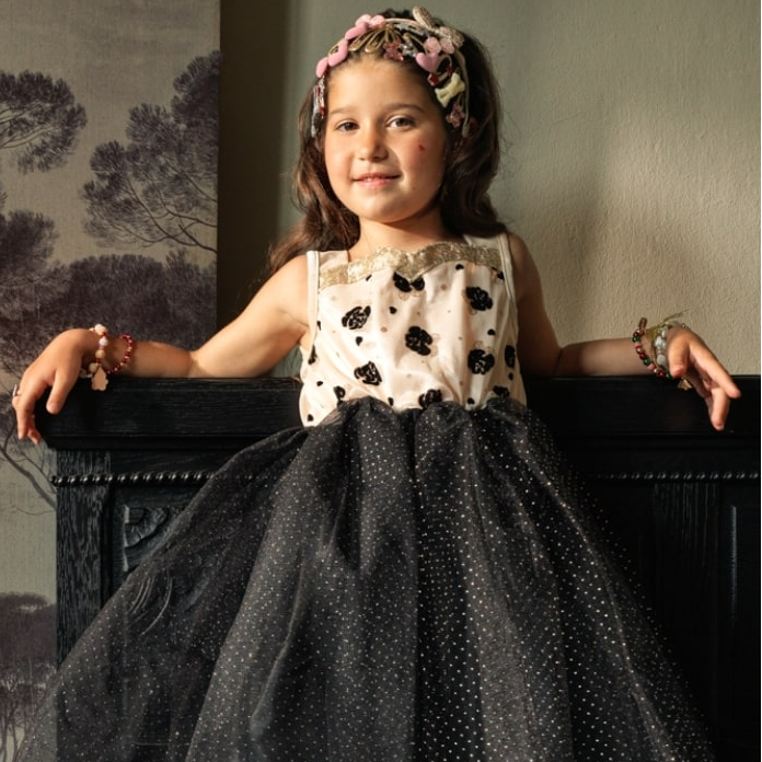 Young girl in a polka dot dress sitting on a bench with a scenic painting in the background