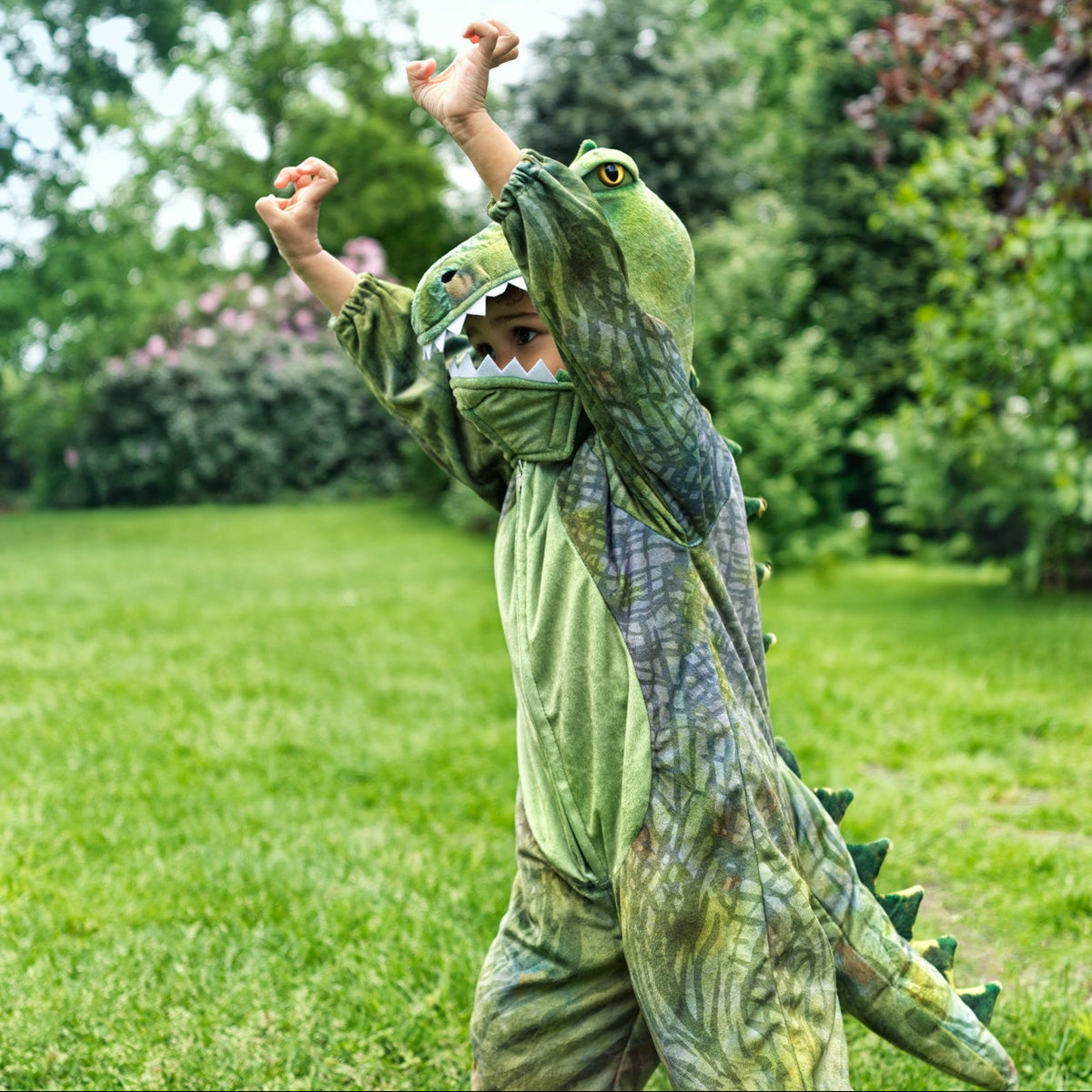 Child in a green dinosaur costume playing outdoors on a grassy area with trees in the background